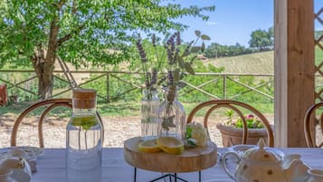 Una tavola apparecchiata con bicchieri, un centrotavola in legno e un teiera, con vista su un vigneto sullo sfondo.