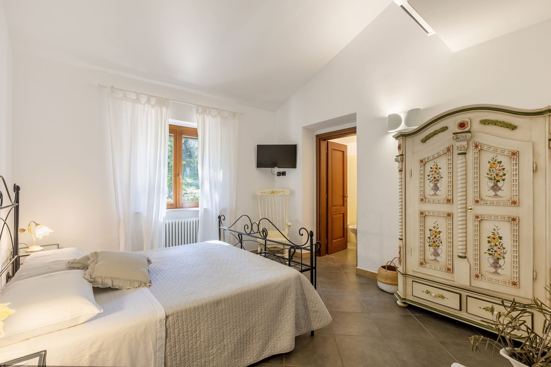 Una camera da letto con un letto, una TV a parete, un termosifone e un armadio decorato con motivi floreali.