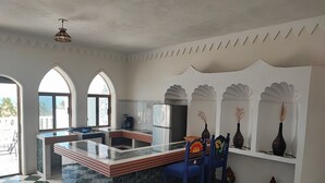 A kitchen with a central island, two blue chairs, a refrigerator, and decorative vases on a shelf. - Ocean view apartment with pool in San Pancho - Casa Blanca (San Francisco)