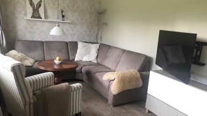 A modern living room with a sectional sofa, a round coffee table, a striped armchair, a television, and a decorative shelf with artwork. - 4 Star Holiday Home in Sydals (Sydals)