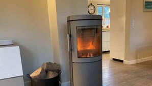 A modern, cylindrical wood-burning stove with a glass door, placed on a black mat in a room with wooden flooring and a white cabinet. - 4 Star Holiday Home in Sydals (Sydals)