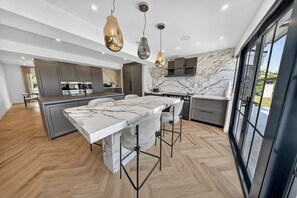 Uma cozinha moderna com bancadas de mármore, uma ilha central com banquetas e iluminação pendente.