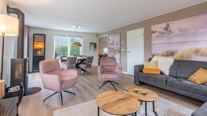 A modern living room with a sofa, two armchairs, a dining table, and a fireplace. - Charming Villa Near the sea and Forest (De Koog)