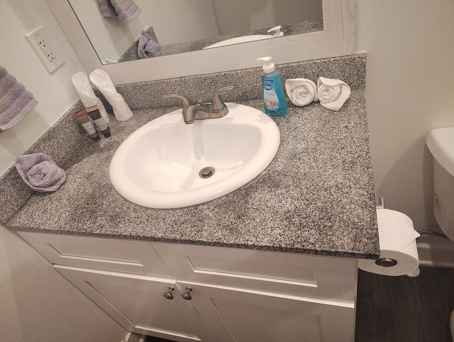 A bathroom with a white sink, granite countertop, and a mirror above it. There are towels and toiletries on the counter.