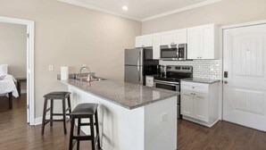 A modern kitchen with white cabinets, a granite countertop, and stainless steel appliances. There are two bar stools and a small island. - Contemporary Hideout - 7min to Clemson University (Central)