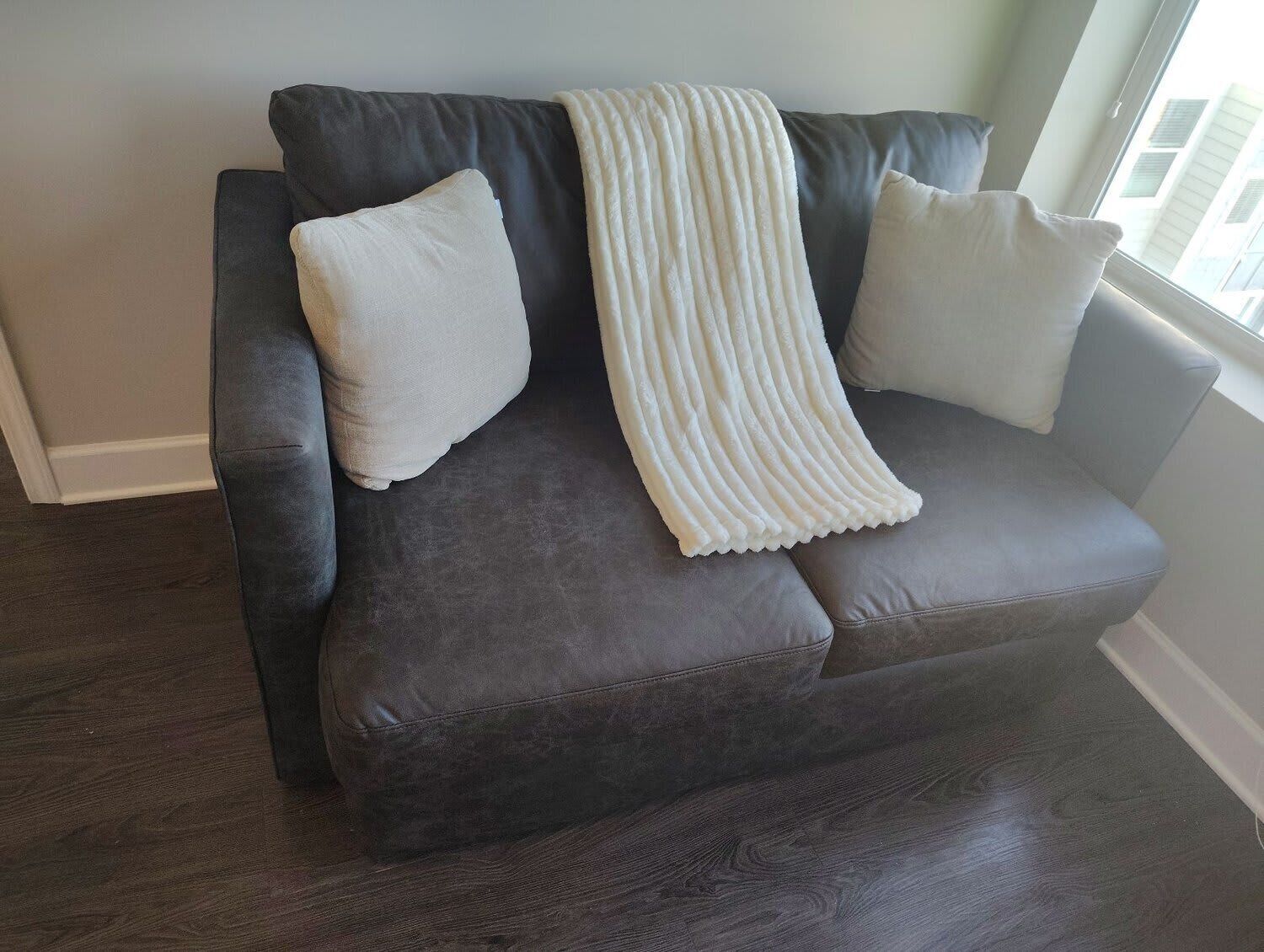 Ein dunkelbraunes Ledersofa mit weißer Decke und zwei weißen Kissen.