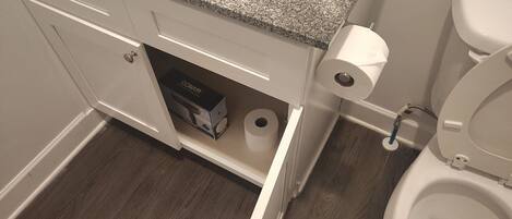 Et badeværelse med en bordplade i granit, et hvidt toilet, en bidet og et skab med en æske mærket "CONAIR".