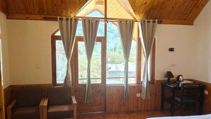 Una cabaña de madera con una cama, un sofá, un escritorio y vistas al exterior a través de amplias ventanas.