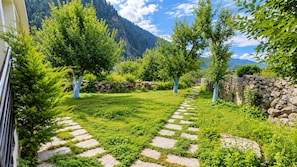 A stone pathway leading through a lush garden with trees and a mountain backdrop. - Pravara Cottages (Manali)