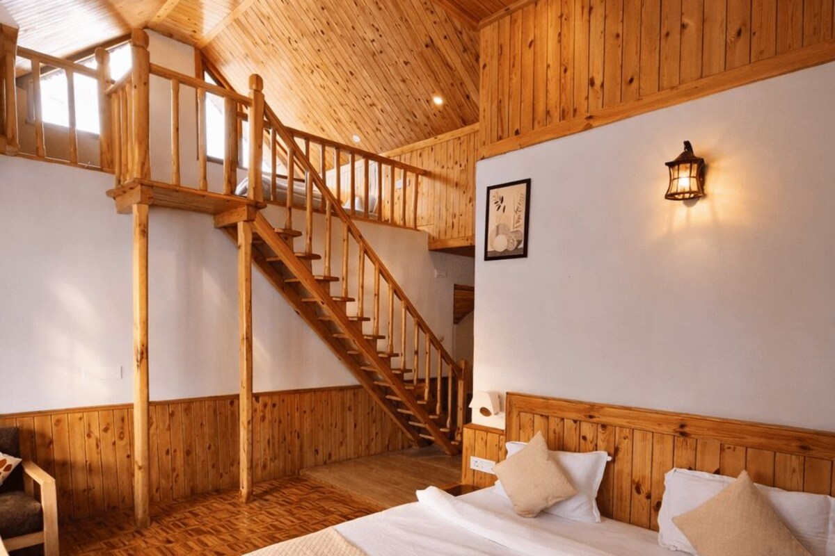 Interior de uma cabana de madeira com cama, escada e luminária fixada na parede.