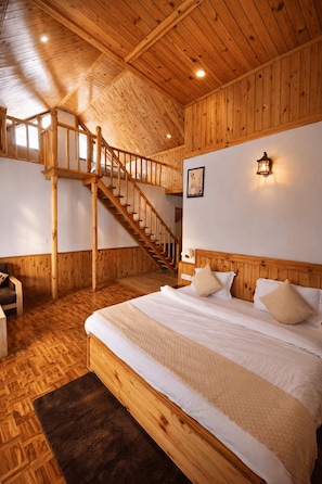 A wooden cabin interior with a bed, a staircase, and a wall-mounted light fixture. - Pravara Cottages (Manali)