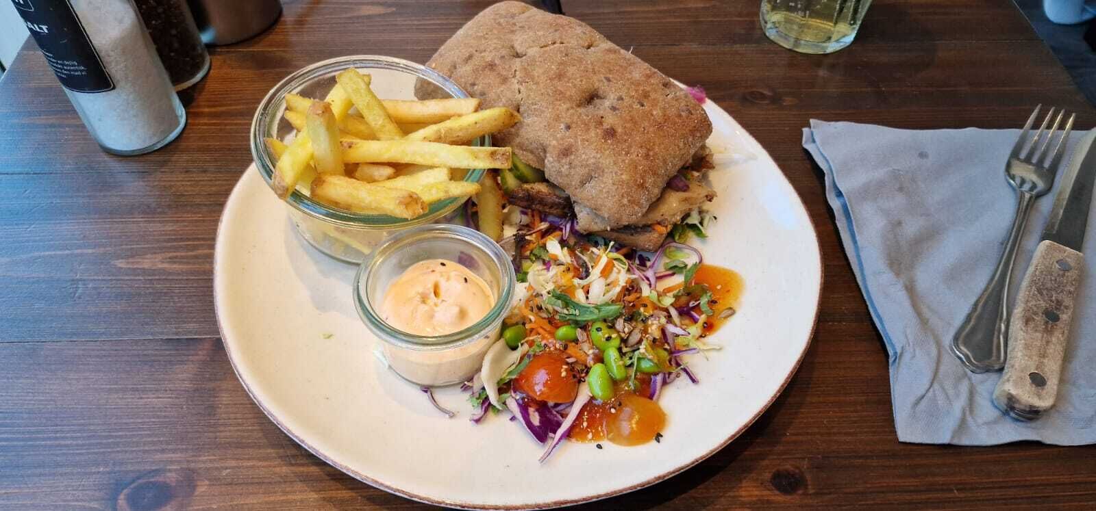 Une assiette avec un sandwich, des frites et une salade accompagnée de sauce.