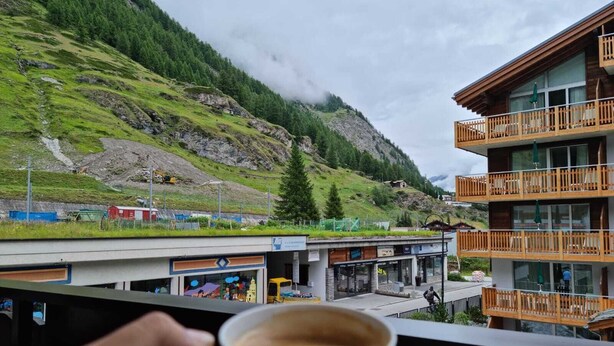 Vista de la montaña con un edificio que tiene balcones y una taza de café al frente.