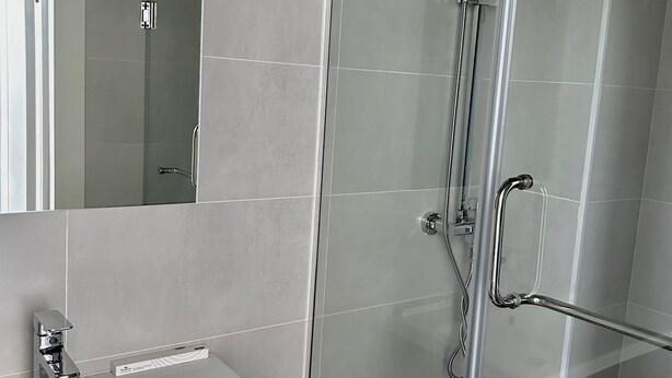 A bathroom with a glass shower enclosure, a white sink, and a mirror. - Elite Hotel (Almaty)