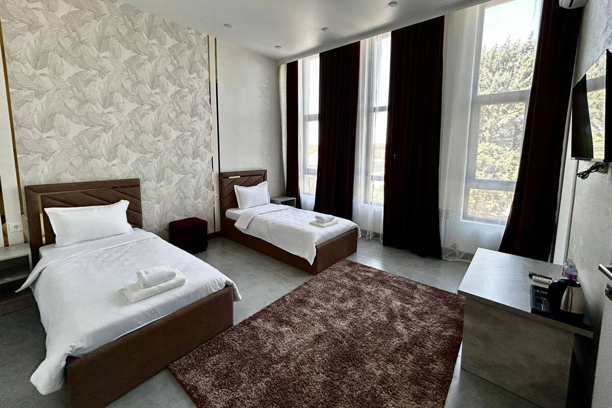 A hotel room with two beds, a large window with curtains, a TV, and a small desk.