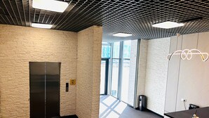 Un ascenseur moderne avec un mur texturé, un comptoir d’accueil agrémenté d’un luminaire décoratif et une vue sur l’extérieur grâce à de grandes fenêtres.