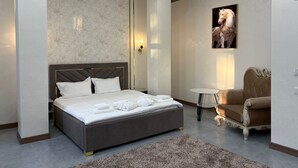 Une chambre moderne avec un grand lit, une petite table ronde, un fauteuil classique et un tableau accroché au mur.
