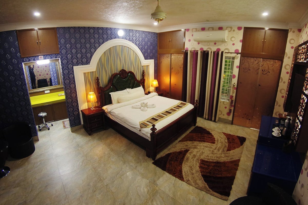 A bedroom with a bed, two bedside tables, a mirror, a wardrobe, and a patterned rug.
