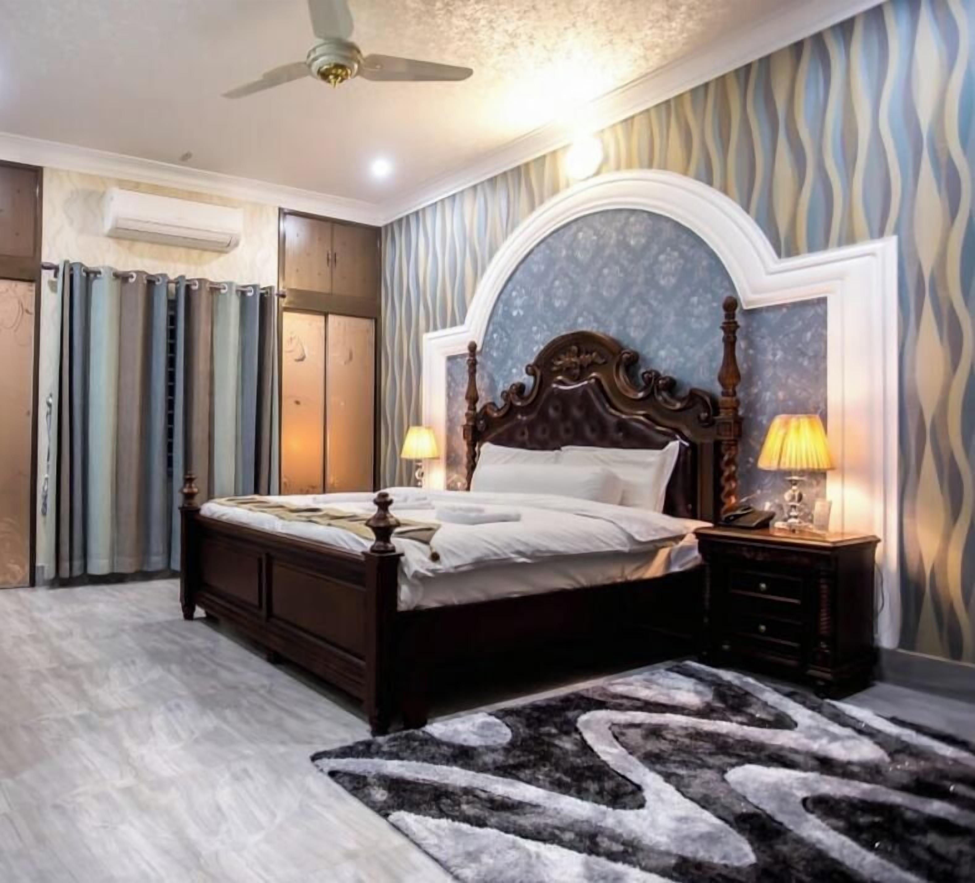 A bedroom with a bed, nightstands, a ceiling fan, and a patterned wall.