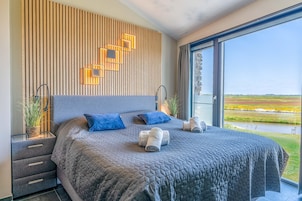 Quarto moderno com uma cama grande, parede de ripas de madeira e vista para uma paisagem verde através de uma janela ampla.