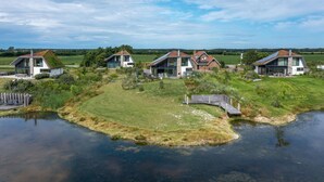 A residential area with modern houses, a pond, and a grassy field. - Modern, Luxurious and Sustainable Nature Villa (De Waal)