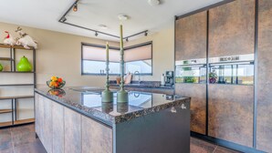A modern kitchen with a central island, built-in appliances, and a large window. - Modern, Luxurious and Sustainable Nature Villa (De Waal)