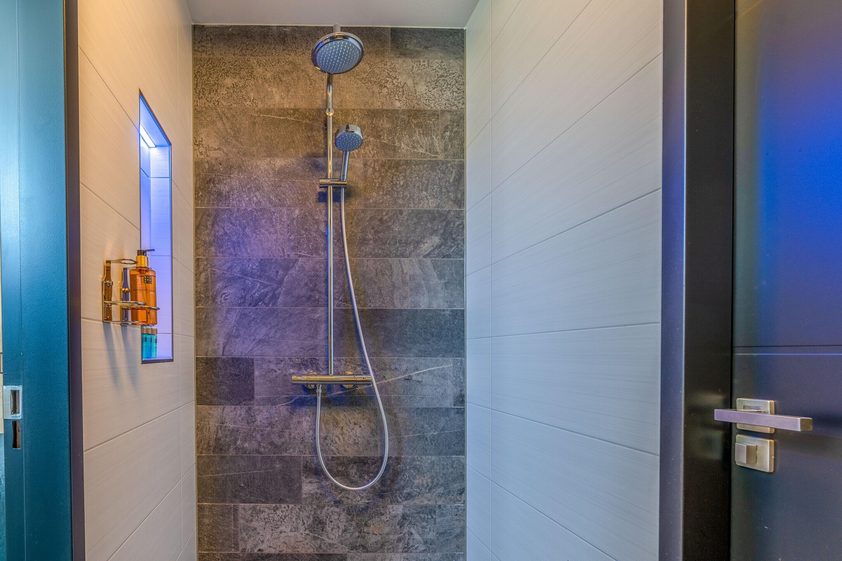 A modern shower with a handheld showerhead and a fixed wall-mounted showerhead, set against a textured stone wall.
