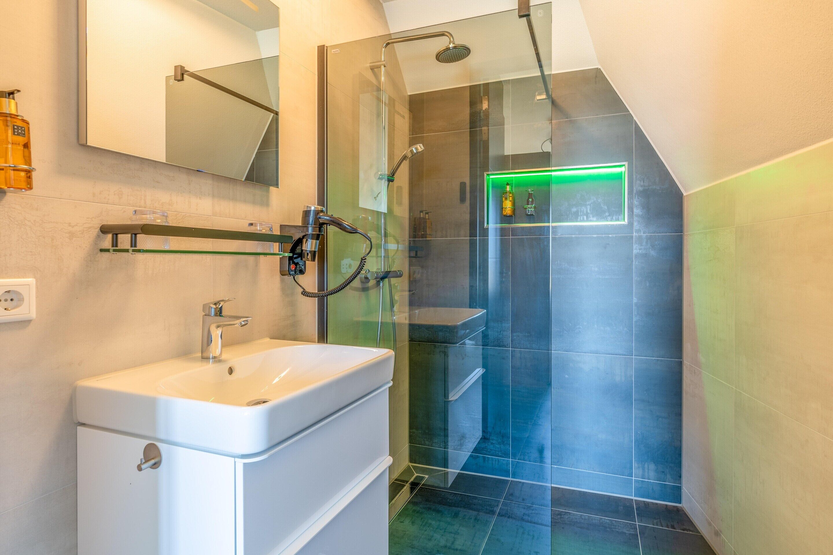 A modern bathroom with a glass-enclosed shower, a white sink, and a mirror above it.
