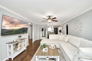 Ein modernes Wohnzimmer mit Ecksofa, Couchtisch, Fernseher und Deckenventilator.