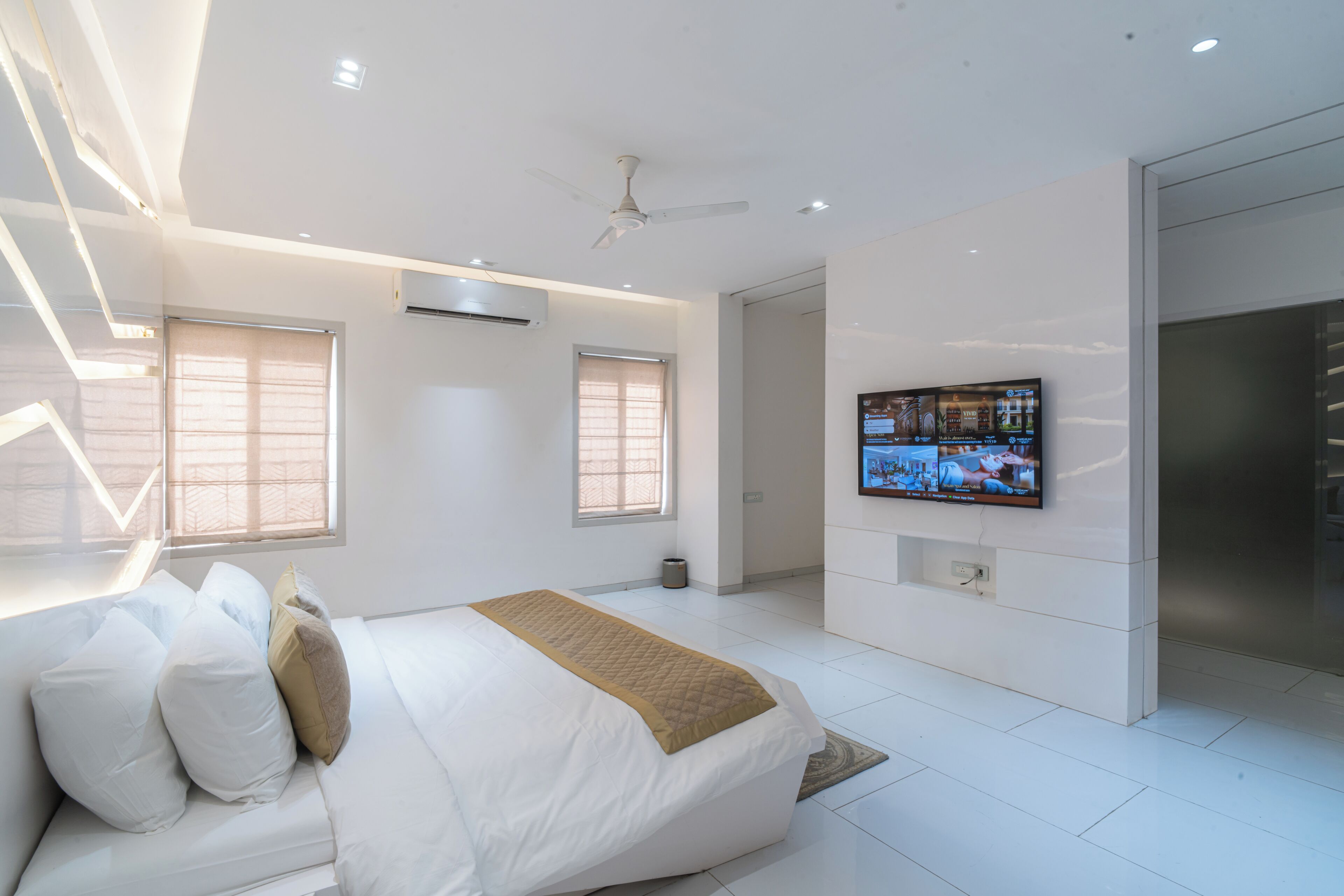 A modern bedroom with a bed, a television on the wall, and a ceiling fan.