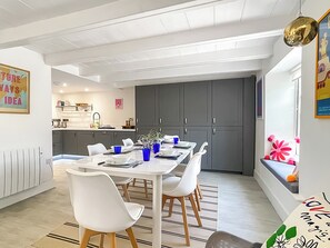 Une cuisine moderne avec des meubles gris, une table à manger blanche avec des chaises et une fenêtre donnant sur l’extérieur.