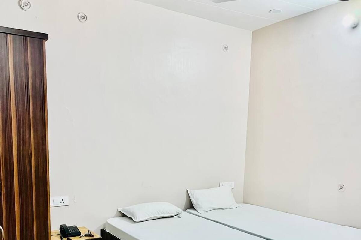 A bedroom with a wooden bed frame, two white mattresses, a small wooden cabinet, and a ceiling fan.