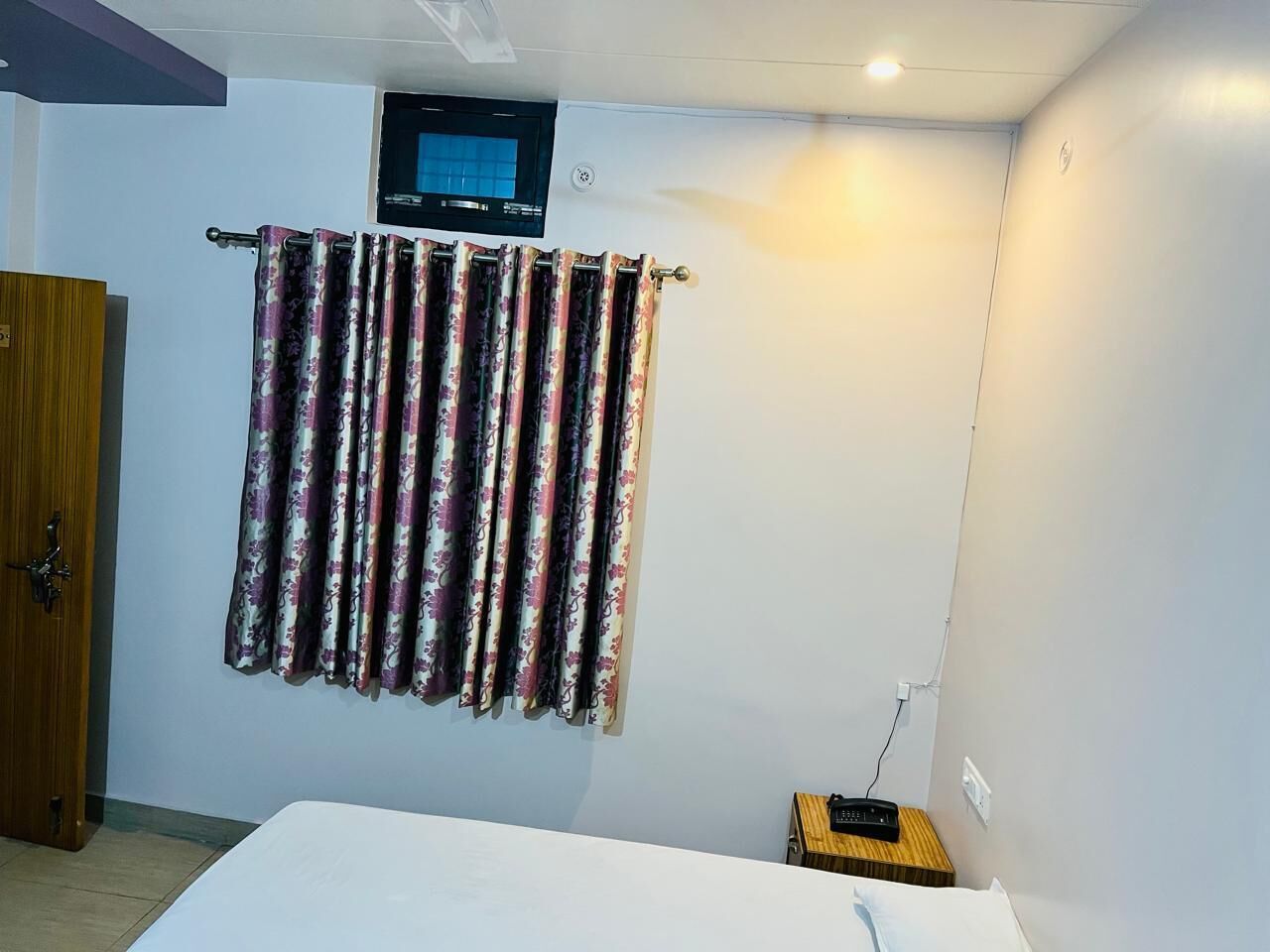 Um quarto com uma cama, uma televisão na parede e uma cortina.