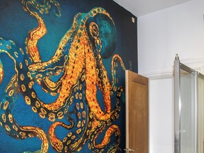 A room with a large octopus mural on the wall, a wooden door, and a white wall.