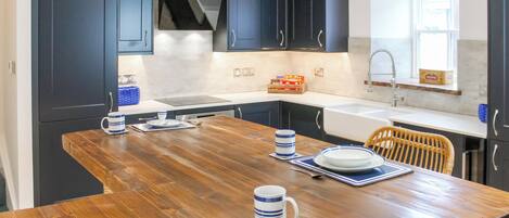A modern kitchen with dark cabinets, a wooden dining table set with plates, bowls, and cups, and a window with a view.