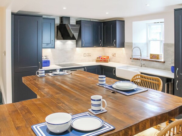 A modern kitchen with dark cabinets, a wooden dining table set with plates, bowls, and cups, and a window with a view.