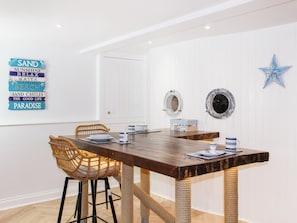 Un comedor con mesa de madera, sillas de mimbre, decoración de temática náutica y un adorno con forma de estrella.