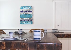 A dining table with a decorative sign, a mug, and a cup on it. - 4 bedroom accommodation in Falmouth (Falmouth)