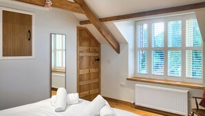 Ein Schlafzimmer mit einem Bett, Holzbalken, einem Fenster mit Jalousien, einem Heizkörper und einem Holzschrank.