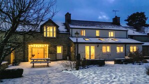 Ein zweistöckiges Haus mit einer Stein-Fassade, einer Holzterrasse und einem mit Schnee bedeckten Rasen.