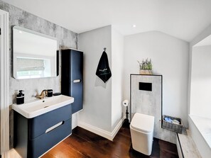 A modern bathroom with a large mirror, dark cabinetry, a white toilet, and a small plant on the wall. - Mill House - UK50646 (Falmouth)