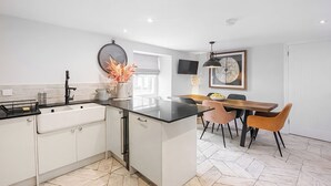 A modern kitchen with white cabinets, a black countertop, and a dining area with a wooden table and chairs. - Mill House - UK50646 (Falmouth)