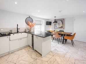 A modern kitchen with white cabinets, a black countertop, and a dining area with a wooden table and chairs. - Mill House - UK50646 (Falmouth)