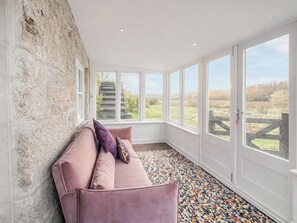 A room with a stone wall, a pink sofa, and large windows with a view of a staircase and greenery. - Mill House - UK50646 (Falmouth)