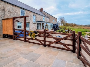 A stone building with a wooden gate, a covered outdoor seating area, and a view of the countryside.
