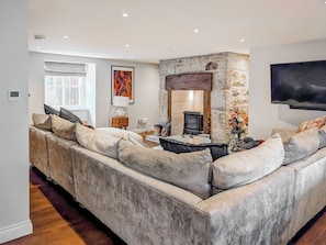 A modern living room with a stone fireplace, a large sofa, a flat-screen TV, and a window with curtains.