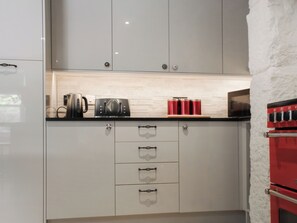 A kitchen with white cabinets, a black coffee maker, red containers, and a red oven. - Mill House - UK50646 (Falmouth)