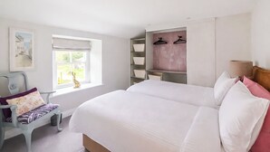 A bedroom with a large bed, a chair, a window, and built-in shelves. - Mill House - UK50646 (Falmouth)