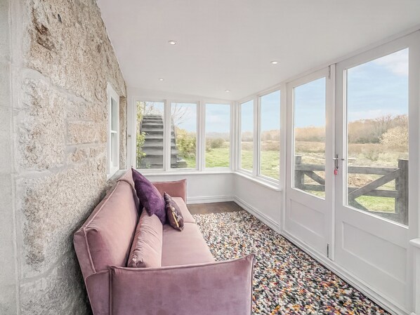 A room with a stone wall, a pink sofa, and large windows with a view of a staircase and greenery.