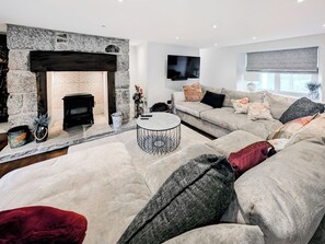 A modern living room with a stone fireplace, a flat-screen TV, a sofa set, and a round coffee table. - Mill House - UK50646 (Falmouth)